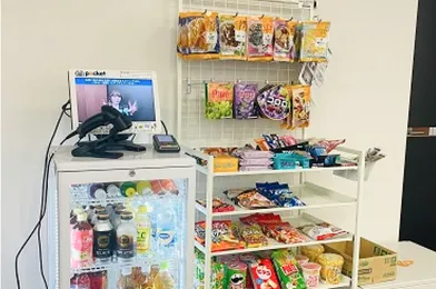 コンビニエンスストアのような売り場。冷蔵庫、お菓子や飲み物の陳列棚、レジ用タブレット端末が見える。