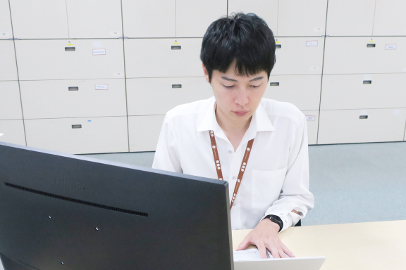 オフィスデスクで、一人の男性がパソコンのモニターとキーボードに向かい、作業に集中して取り組んでいる様子。