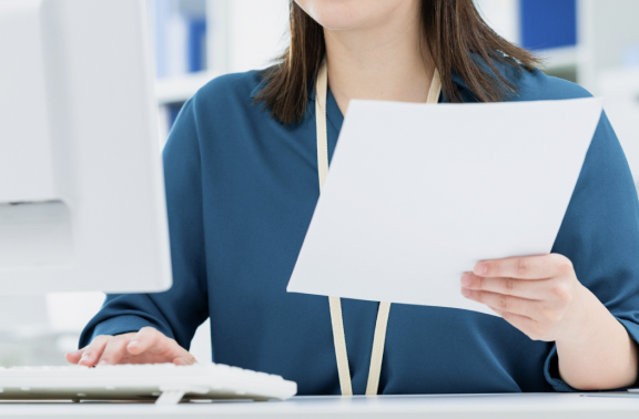 オフィスでパソコンを操作しながら書類を確認する女性